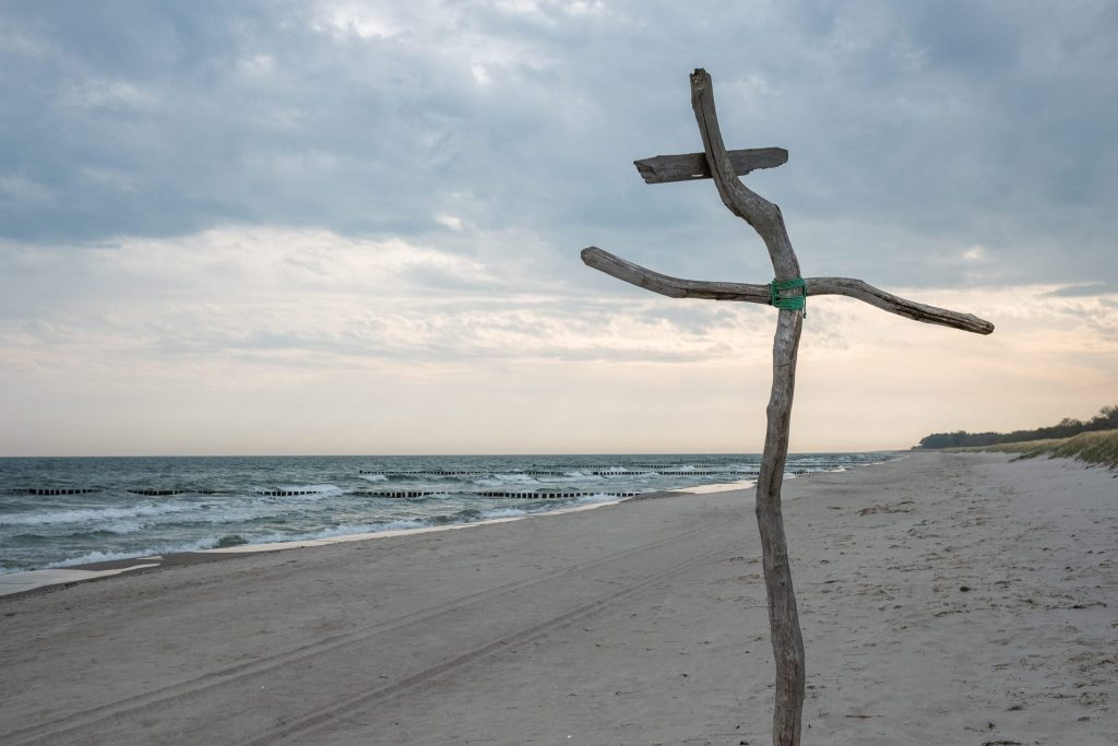 Links die etwas stürmische Ostsee, rechts der Ostseestrand von Zingst und ein krummes Holzkreuz.