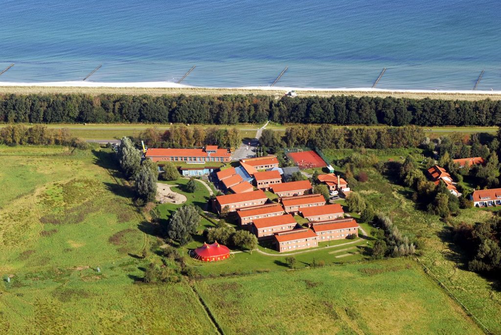 Die Ostseeklinik Zingst in einer Luftaufnahme. Man sieht das Gebäude und das Gelände mit dem Zirkuszelt darauf und die Nähe zum Strand.