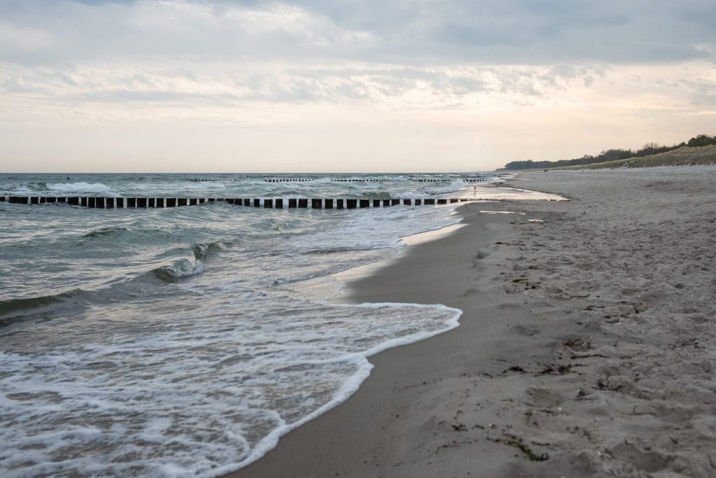 Links die etwas stürmische Ostsee, rechts der Ostseestrand, darüber ein bedeckter Himmel.