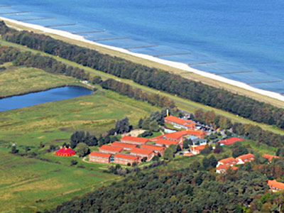 Luftaufnahme der Ostseeklinik Zingst, eingebettet in die grüne Küstenlandschaft, rechts davon die blaue Ostsee.